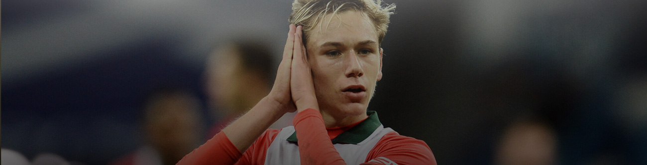 Молодой футболист на поле, сложив руки вокруг головы, стоит в спортивной форме против размытого фона стадиона